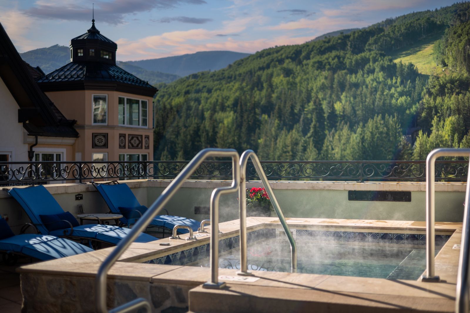 Steaming rooftop hot tub with lounge chairs overlooking forested mountain slopes, hospitality photography in Colorado