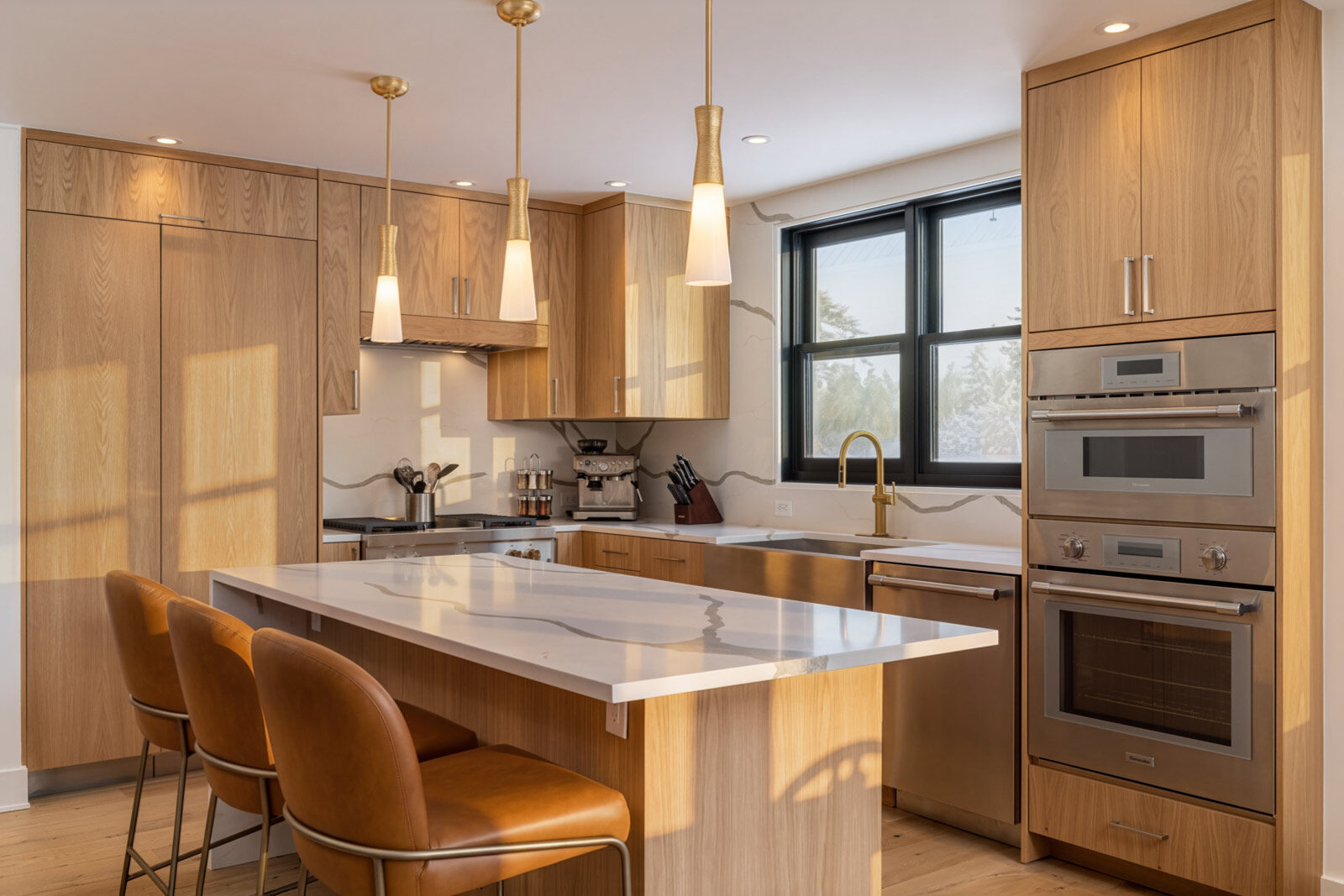 White oak kitchen with an island, brass pendants and leather stools. Mountainside Retreat, Telluride, CO